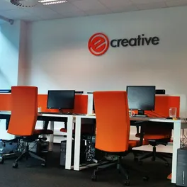 Das eCreative-Büro in Danzig: offener Raum mit orangefarbenen Stühlen und dem Studio-Logo an der Wand